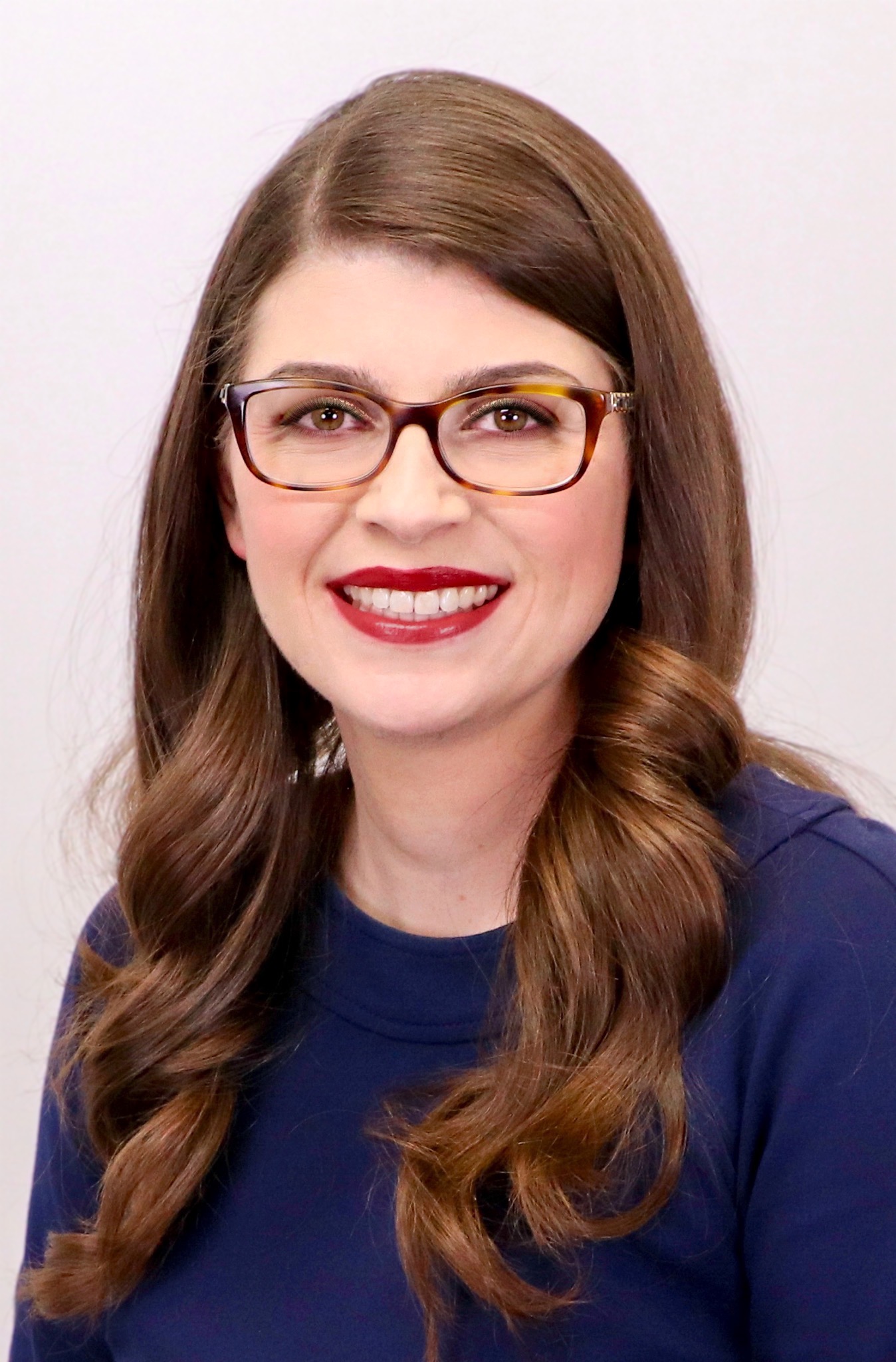 Woman with brown hair, glasses, and a navy blue top smiling.